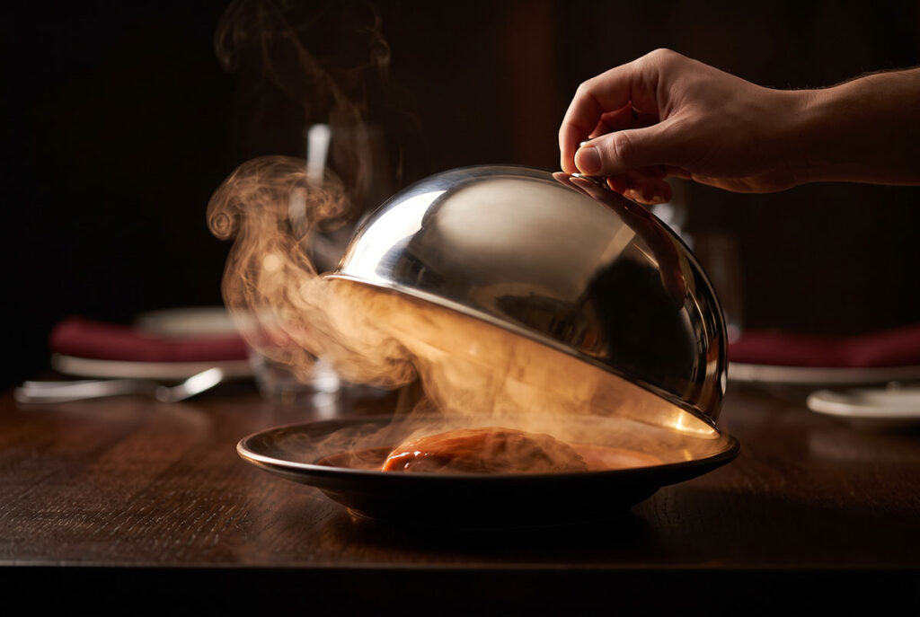 Partially lifted cloche with steam escaping illustrates the sensory gap that makes audiences complete the message
