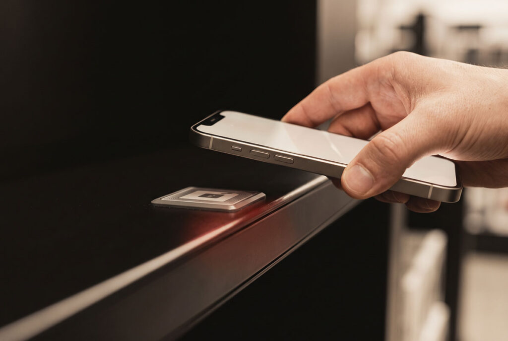 A hand holds a phone a few centimeters from an NFC tag, isolating the deliberate physical gesture behind a tap.