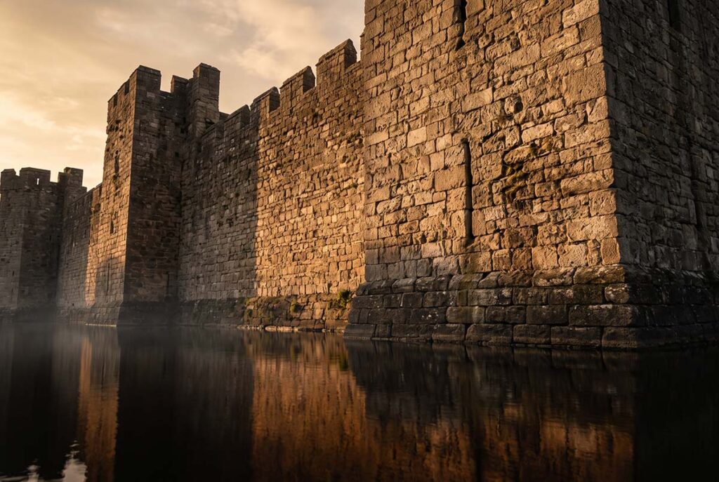 Stone castle moat wall with still water in amber late-afternoon light, representing identity as a competitive moat that compounds rather than erodes