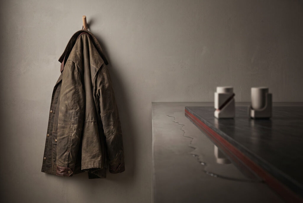 A worn jacket hangs near a dark reflective surface, suggesting proof and sacrifice as the source of brand trust.